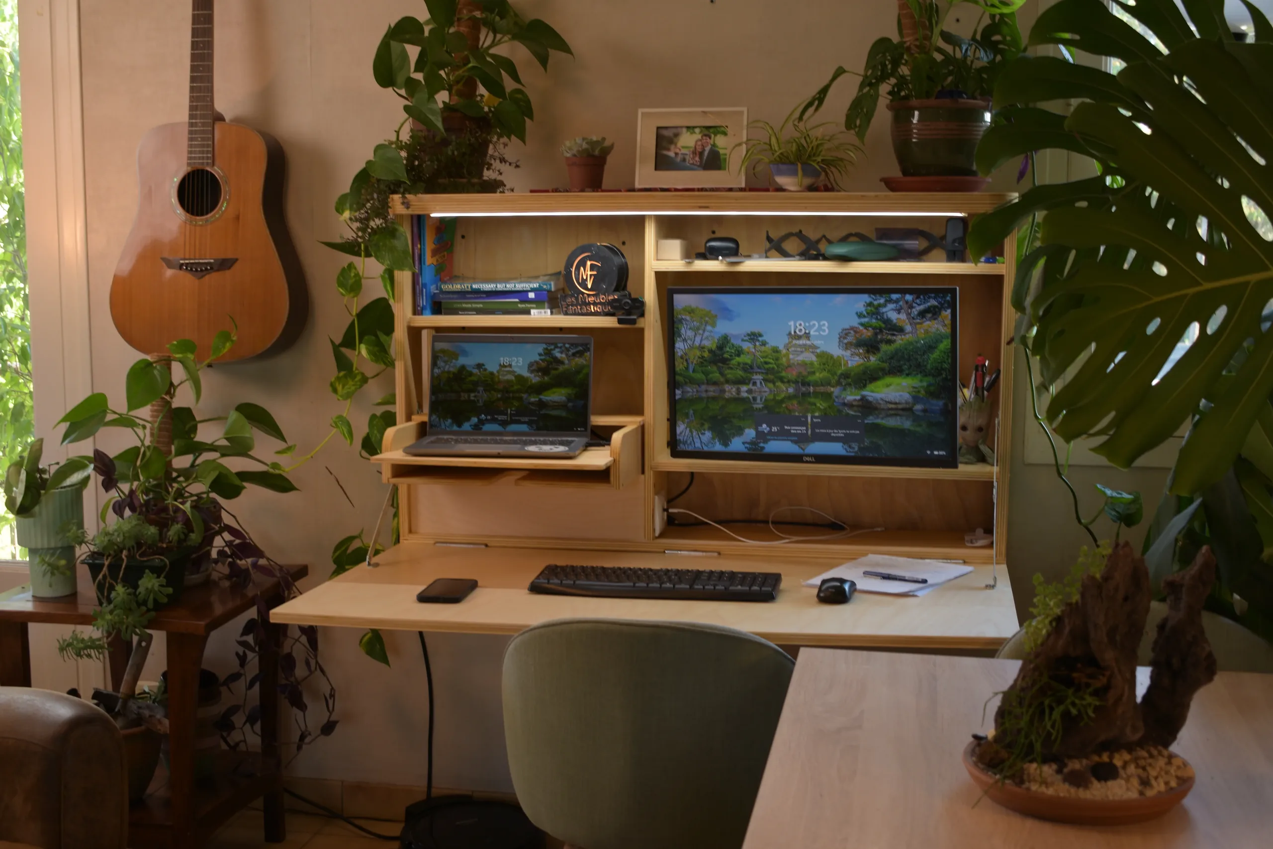 Bureau mural rabattable ouvert avec ordinateur portable, écran et clavier, dans un salon avec des plantes