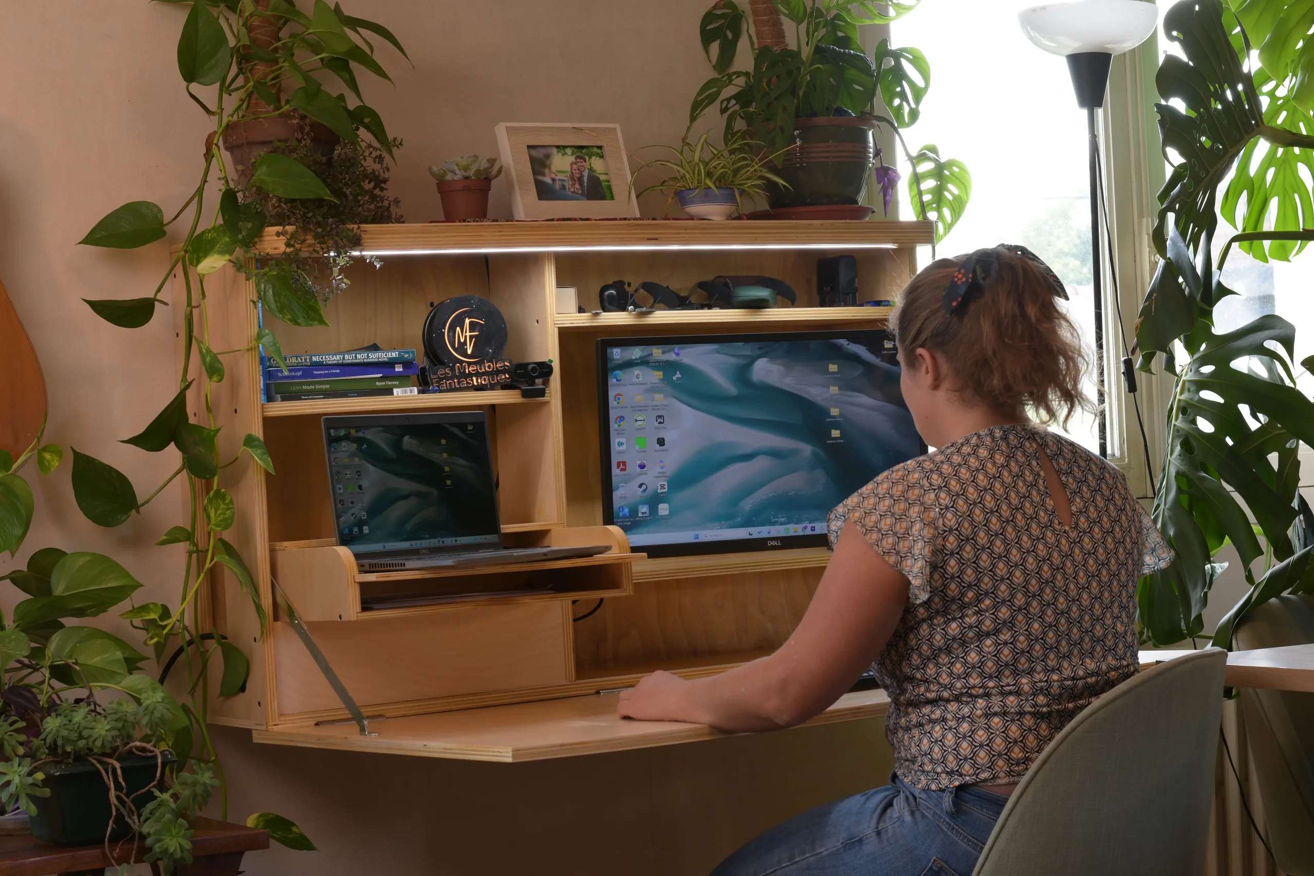 Une femme travaille à son bureau mural rabattable ouvert, avec ordinateur portable et grand écran